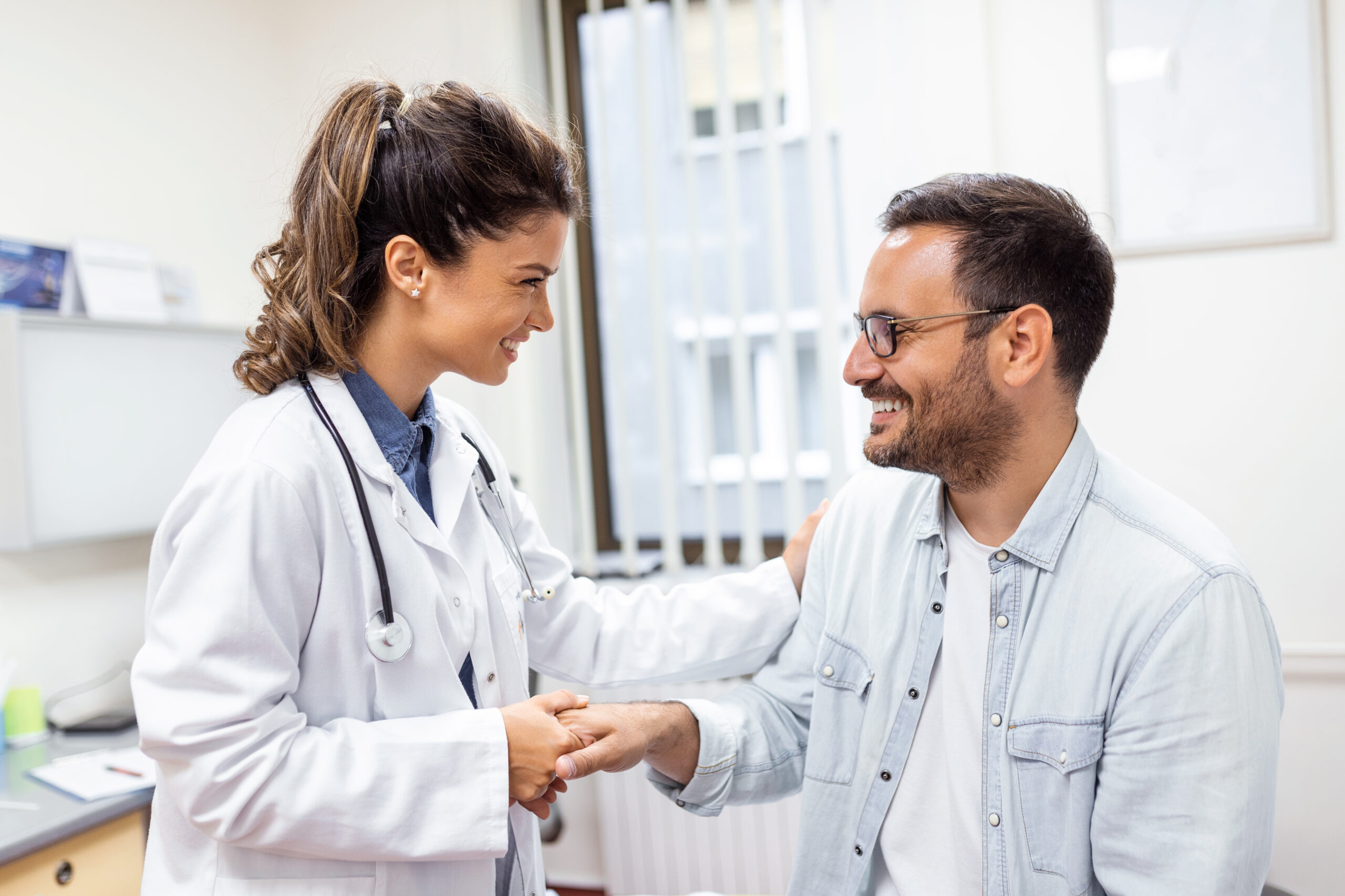 Young woman doctor or GP in white medical uniform consult male patient in private hospital. Female therapist speak talk with man client on consultation in clinic.